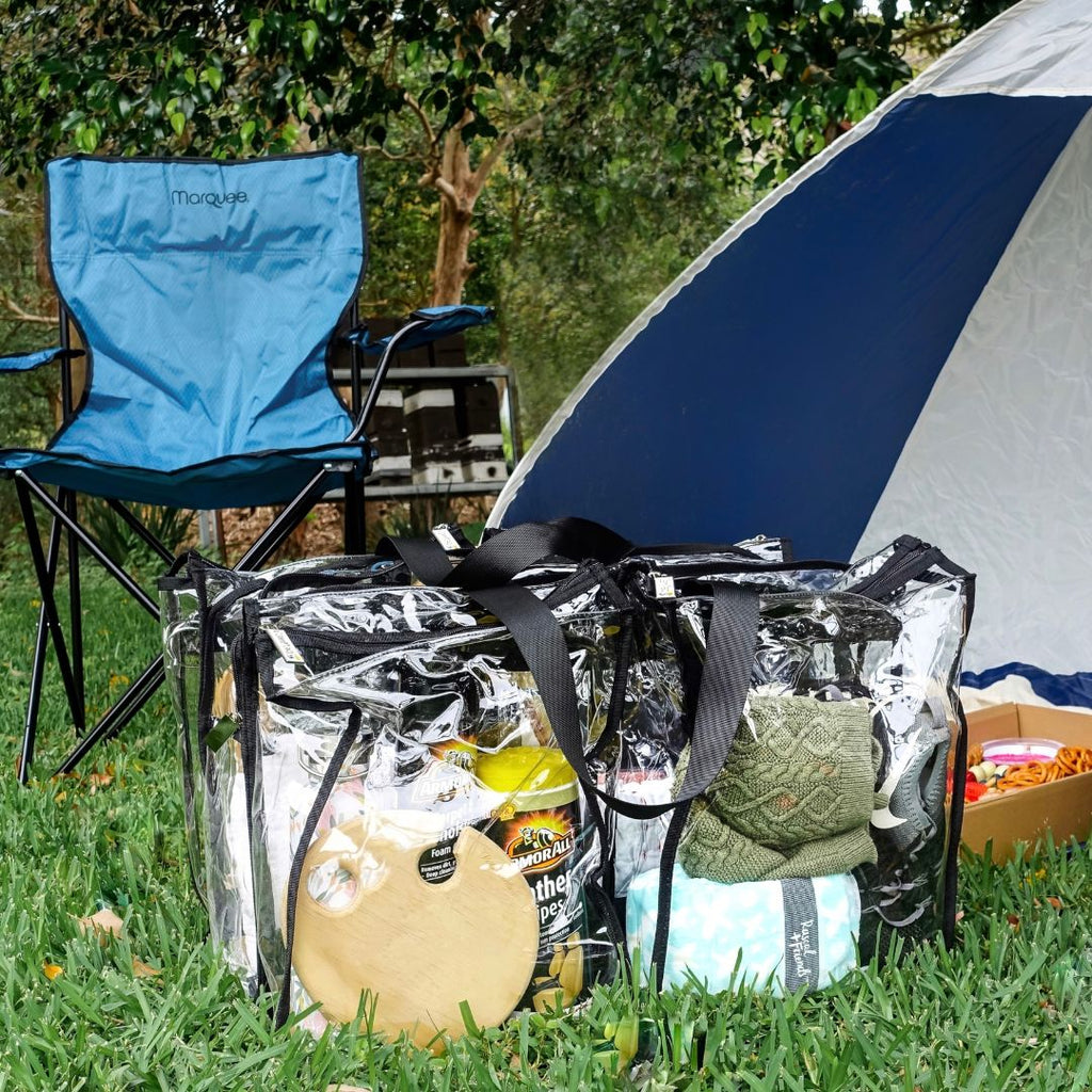Clothes and camping items packed into large black CamPaq clear bag sitting outside tent and camp chair