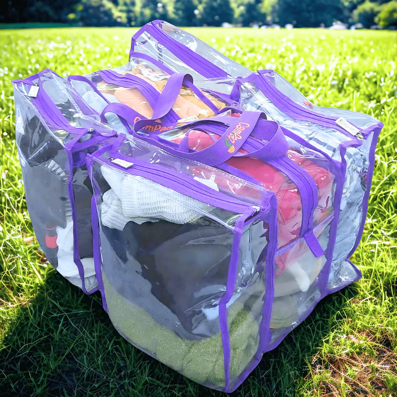 Large clear camping bag with purple zippers containing clothes on a grassy field