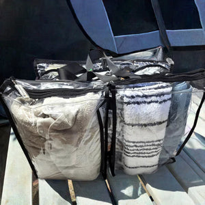 Large black trim clear camping bag packed with with linen beside tent