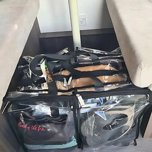 Large black trim clear camping bag with packed with clothes sitting on floor underneath camper trailer table