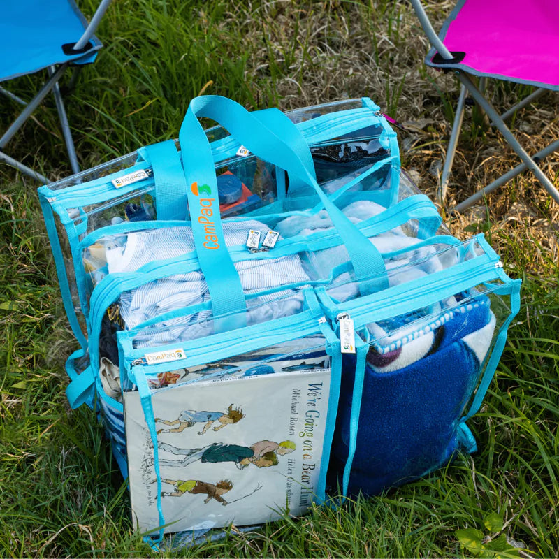 Medium clear blue camping bag with books and towels on grass
